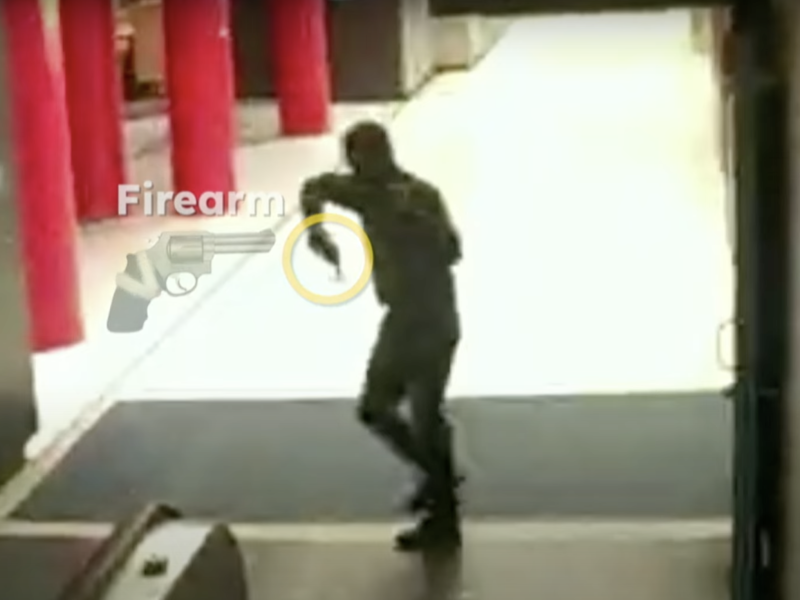 A person is walking indoors while holding a firearm. Location appears commercial, with red pillars and an escalator visible. An on-screen label highlights the firearm.
